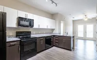 Modern kitchen with sleek dark cabinets, granite countertops, and stainless steel appliances, leading to a bright, open-concept living area.