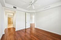 Bright, airy bedroom with elegant wood flooring and a ceiling fan, leading to a modern bathroom with sleek tile design.