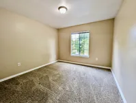 Bright and inviting bedroom with plush carpeting and a large window showcasing a peaceful greenery view.