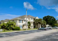 Charming apartment complex with lush palm trees, ample parking, and clear blue skies.