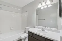 Modern and bright bathroom featuring sleek fixtures, a pristine bathtub, and a spacious vanity mirror, perfect for relaxation.