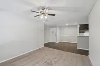 Inviting living space featuring plush carpet, sleek hardwood floor transition, and modern ceiling fan in an open layout apartment.
