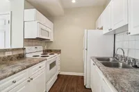 Modern apartment kitchen featuring sleek white cabinetry, stylish countertops, and stainless steel appliances, including a microwave and electric stove.