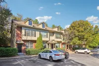 Charming townhouse exterior surrounded by lush greenery, featuring modern architecture with dormer windows and ample parking space.