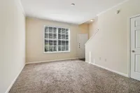 Bright and inviting living room with plush carpeting, large window for natural light, and a modern entryway design.