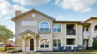 Charming two-story apartment building with elegant balconies and stone accents, set against a bright blue sky.