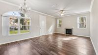 Inviting living room with elegant chandelier, large sunlit windows, and cozy fireplace, featuring sleek hardwood flooring.