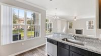 Bright and inviting living area with stylish granite countertops, modern chandelier, and large windows overlooking a serene neighborhood view.
