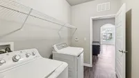 Modern laundry room with sleek white washer and dryer, featuring open shelving and view into sunlit living area with large window.