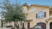 Charming townhouse exterior with a Mediterranean design, featuring stucco walls, arched windows, and a welcoming driveway.