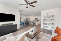 Inviting open-concept living area featuring a modern kitchen, elegant dining space with blue chairs, and a cozy living room with stylish decor and a ceiling fan.