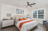 Bright and inviting bedroom with modern decor, featuring a plush bed with vibrant pillows, elegant bedside lamps, and large windows letting in natural light.