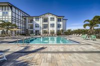 Luxurious apartment complex with a pristine outdoor pool area, surrounded by stylish loungers and palm trees under a clear blue sky.