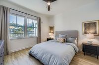 Inviting bedroom with contemporary decor, featuring a large window with a lush outdoor view, a plush bed with elegant pillows, and warm ambient lighting.