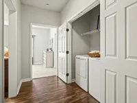 Inviting apartment hallway with laundry nook featuring washer and dryer, leading to a cozy bedroom.