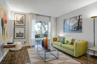 Chic living room with elegant decor, featuring vibrant artwork, stylish green sofa, and natural light from large sliding glass doors opening to a patio.