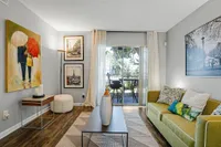 Charming living room with contemporary art, cozy green sofa, and a glass door leading to a scenic balcony.