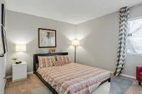 Cozy bedroom with modern decor, featuring a plaid-patterned bed, stylish lamps, and a window with natural light.
