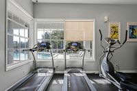 Modern fitness center with treadmills and an elliptical overlooking a sunlit pool area, ideal for energizing workouts.