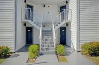 Modern apartment entry with a striking staircase and stylish blue doors, accented by well-maintained greenery.