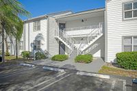 Charming white two-story apartment building with lush green landscaping and modern stairway access, offering serene outdoor parking space.