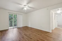 Bright and airy living space with modern wood flooring, ceiling fan, and sliding doors opening to a scenic balcony view.