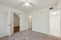 Bright and inviting bedroom with plush carpet, featuring an entrance to an adjacent wooden-floored room and a modern bathroom.