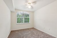 Bright and airy bedroom with a large window offering serene views of green trees, featuring soft carpeted flooring and a modern ceiling fan.
