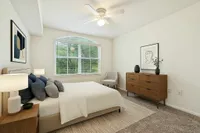 Bright and inviting bedroom with a cozy bed, elegant wooden dresser, modern artwork, and large window offering lush green views.