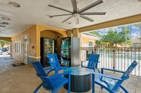 Inviting outdoor lounge area with vibrant blue chairs and a ceiling fan, overlooking a sparkling pool through elegant fencing.