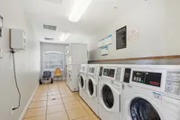 Bright laundry room featuring multiple washers and dryers, modern lighting, and comfortable seating area by the window.