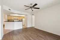Modern apartment living area with elegant wood flooring, ceiling fan, and an open-plan kitchen with sleek cabinetry.
