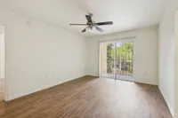 Bright, open living room with elegant wood flooring, ceiling fan, and sliding glass doors leading to a scenic balcony view.