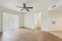 Bright living area with sleek hardwood floors, modern ceiling fan, and large windows offering natural light.