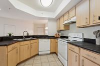 Modern kitchen with sleek black countertops, light wood cabinets, and a complete set of appliances, showcasing stylish functionality.