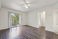 Bright living area with elegant wood flooring, ceiling fan, and sliding glass doors opening to a lush green view.