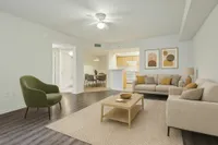 Bright and inviting living room with modern decor, featuring a cozy seating area, stylish green accent chair, and open access to a sleek kitchen and dining area.