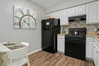 Charming kitchen with modern black appliances, sleek white cabinets, and a cozy dining nook under a stylish clock decor.