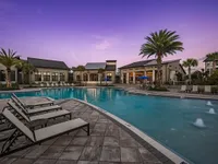 Luxurious apartment complex with a stunning outdoor pool, surrounded by palm trees and sun loungers under a vibrant purple sunset sky.