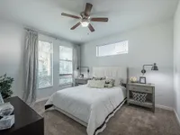 Bright and inviting bedroom with large windows, modern ceiling fan, and cozy decor creating a serene atmosphere.