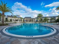 Luxurious apartment complex with inviting round outdoor pool, surrounded by palm trees and modern lounge chairs, set against a bright blue sky.