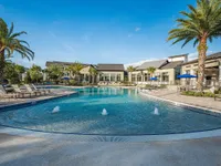 Luxurious apartment complex featuring a stunning resort-style pool surrounded by lounge chairs, palm trees, and modern amenities.