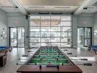 Vibrant recreational room featuring a foosball table and pool table with large sliding glass doors opening to a sunlit patio.
