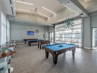 Bright and modern games room featuring pool tables, foosball, and stylish seating with large windows for natural light.