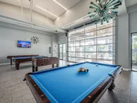 Chic recreation room with a vibrant blue pool table, foosball, and stylish lighting, offering a perfect space for relaxation and entertainment.