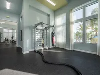 Spacious fitness area with modern gym equipment, boxing setup, and large windows offering a refreshing view of palm trees and a pool.