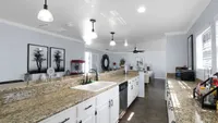 Spacious and modern kitchen with granite countertops, stylish pendant lighting, and open floor plan leading to a cozy living area.