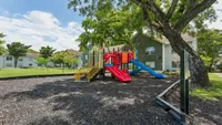 Charming apartment complex featuring a colorful children's playground surrounded by lush greenery and mature trees.
