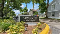 Inviting entrance of Advenir at San Tropez, surrounded by lush greenery and vibrant landscaping.