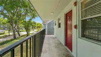 Inviting apartment balcony with charming red door, overlooking a tranquil tree-lined street for peaceful living.